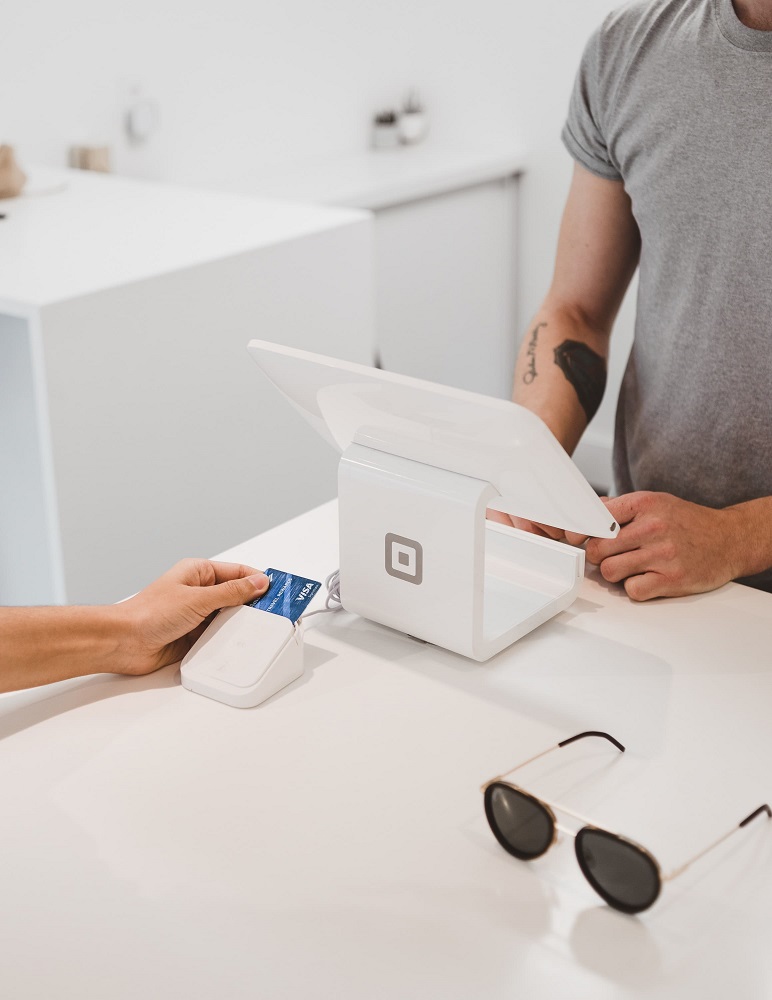 A retail guest waits at the front desk while an attendant inserts his card into a credit card reader. Source: Clay Banks on Unsplash (Zenoti blog post, October 19, 2022). 