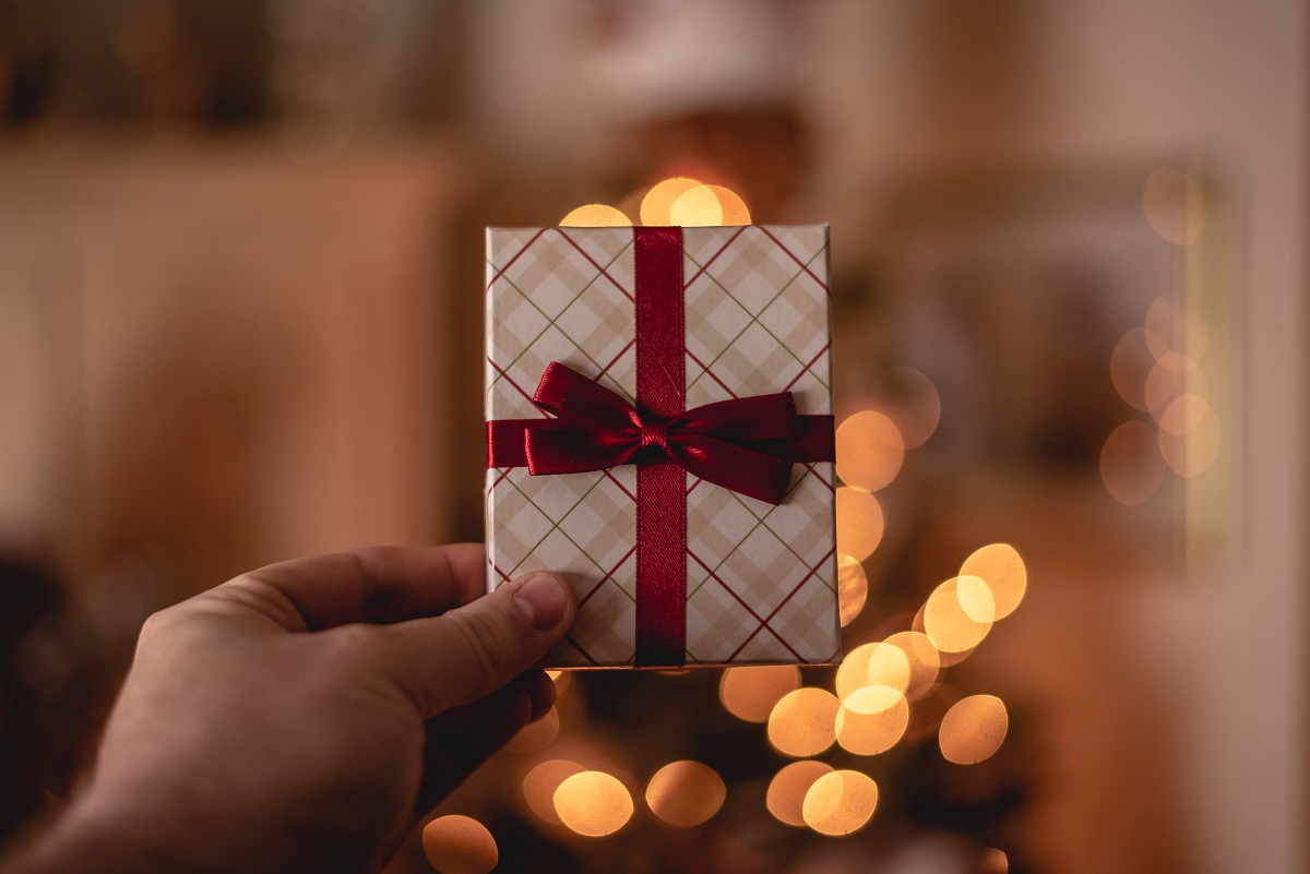 A person holds a box-shaped gift card tied with a red bow, with holiday lights in the background. Source: Rob Laughter on Unsplash  Zenoti blog post, Oct. 21, 2022 